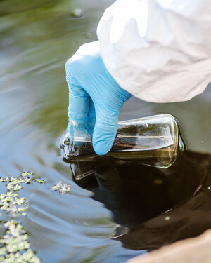 A hand is reaching to scoop water into a glass flask